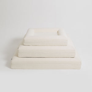 Three different sizes of cream bouclé Mello bolster dog beds stacked on top of each other