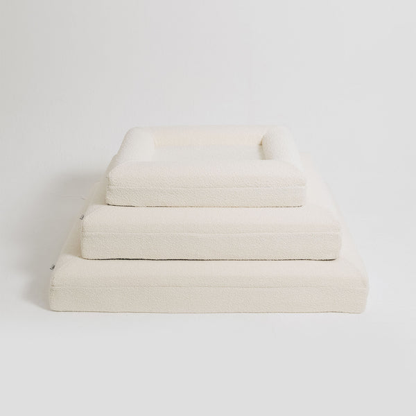 Three different sizes of cream bouclé Mello bolster dog beds stacked on top of each other